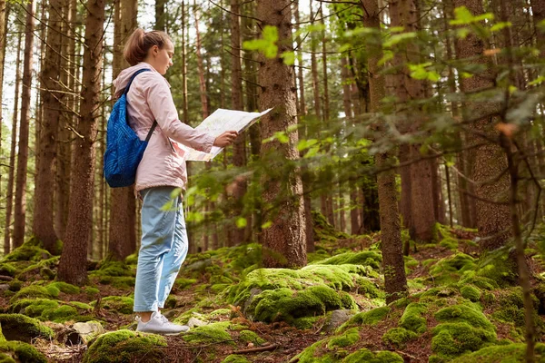 Profilo di giovane donna caucasica con zaini blu e mappa perdersi nella foresta, escursionista guardando la mappa e cercare di trovare il modo, viaggiando in tutto il mondo. Viaggiare, avventura, arrivare concetto di riposo . — Foto Stock