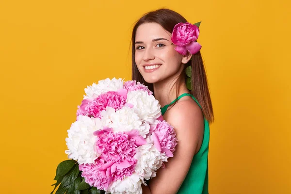Imagen de una joven morena alegre y guapa mirando directamente a la cámara, poniendo flores en el cabello, estando en un ambiente romántico, sosteniendo un gran ramo de flores blancas y rosas. Concepto de personas y regalos . —  Fotos de Stock