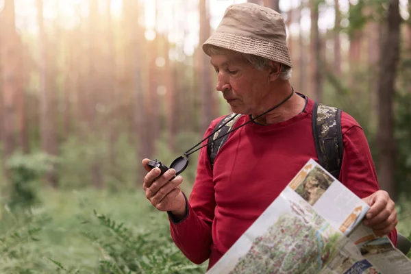 Outdoor shot di uomo anziano che partecipa a gare di orienteering trail, essendo partecipanti al concorso, cerca di trovare il modo, utilizzando mappa e bussola. Viaggiare, avventura e concetto di zaino in spalla . — Foto Stock