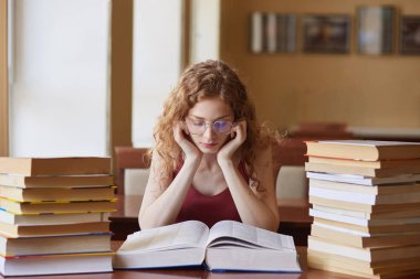 Kızarıklık odasında oturan kadın gencin görüntüsü, bayan okuma kitabı, final muayenesi için hazırlık, bilgi bulma, yüz ifadesini yoğunlaşmış. Öğrenciler ve knowladge kavramı.