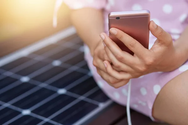 Image d'une femme sans visage en robe rose chargeant son téléphone intelligent sur un chargeur de panneau solaire polyvalent gratuit. Technologie moderne, énergie gratuite pour tous, électricité allternative, concept d'écologie . — Photo