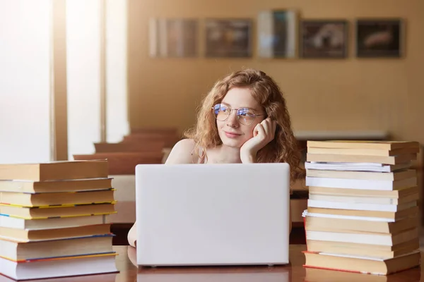 Indoor shot of thoughtful beautiful cute lady looking out of window, dreaming about something, having stop for rest, putting her hand under chin, working with laptop, generating ideas in her mind. — Stock Photo, Image