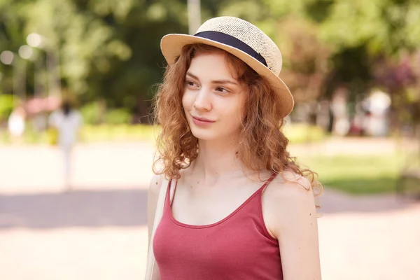 Retrato de close-up de senhora sorrindo bonito ter andar no parque no dia de verão, estar em bom humor, vestindo chapéu com faixa preta e top vermelho, olhando para o lado. Conceito de pessoas e atividades de tempo livre . — Fotografia de Stock