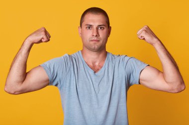 Yakışıklı atletik genç adam kaslarını gösteren Kapalı stüdyo çekim, kollarını kaldırarak, doğrudan kameraya bakarak, emin ve sakin olmak, rahat mavi tshirt giyiyor. İnsanlar ve spor konsepti.