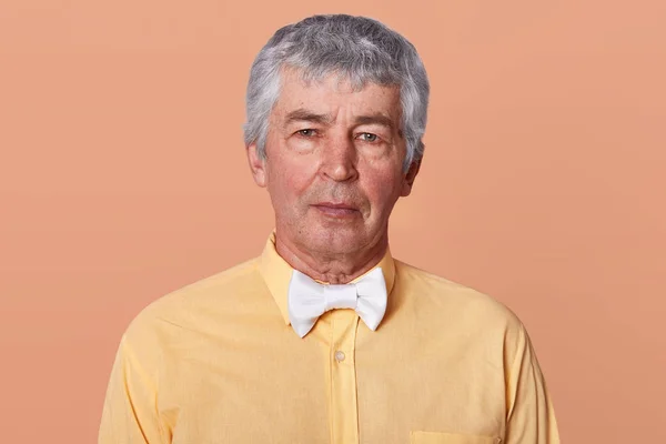 Retrato de estudio interior de hombre serio de pelo gris mirando directamente a la cámara, con camisa amarilla y corbata blanca, con expresión facial tranquila, posando en interiores, aislado sobre fondo de estudio —  Fotos de Stock