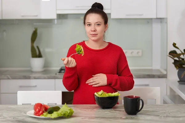 Mujer embarazada joven que come en la cocina en casa, mujer le gusta ensalada verde fresca, señora necesita comer muchas verduras diferentes durante el embarazo, embarazo saludable, maternidad y el concepto de estilo de vida . — Foto de Stock