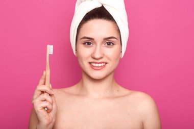 Avrupalı kadın ile yenilenmiş kadın yakın portre elinde diş fırçası tutar, çıplak omuzları ile pozlar, kafasına sarılmış beyaz havlu, pembe arka plan üzerinde izole. Sabah rutin kavramı.