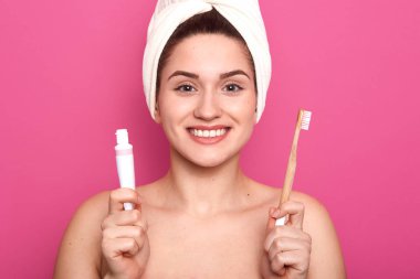 İyi görünümlü büyüleyici bayan içtenlikle gülümseyerek, her iki elinde beyazlatma diş macunu ve ahşap diş fırçası tüp tutan, doğrudan kamera bakarak, yüksek ruhları olmak. Diş bakımı konsepti.