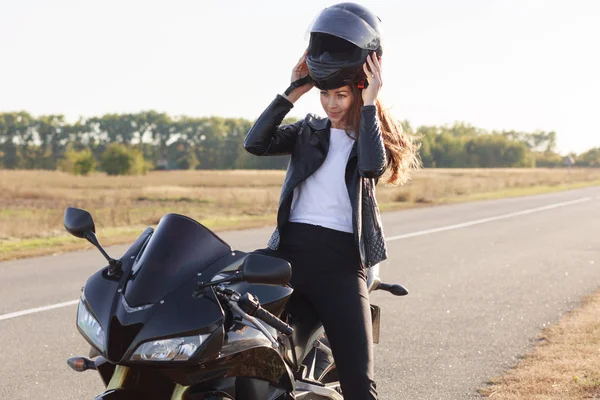 그녀의 오토바이에 앉아 아름다운 날씬한 젊은 위험 테이커의 이미지, 그녀의 차량에 여행을 가지고, 극단적 인 활동을 좋아, 헬멧을 착용, 도로의 측면에 서. 오토바이 관광 개념. — 스톡 사진