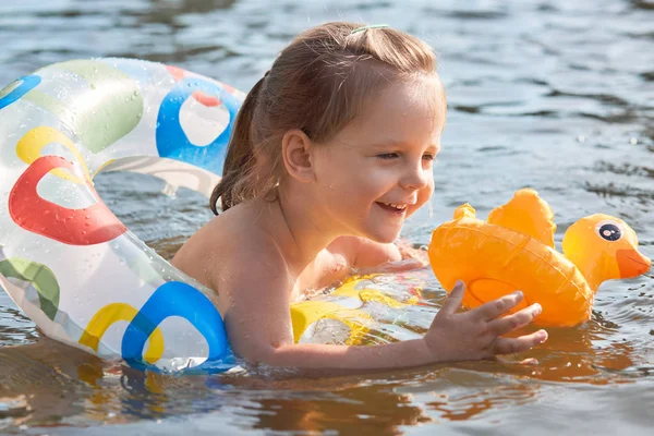 Lifebuoy에서 liitl 소녀의 야외 촬영, 연못에서 수영하는 행복한 아이, 강에서 재미있게 즐기는 고무 링의 토들러, 노란 오리를 잡고, 아이는 행복한 표정을 가지고 있으며, 부모와 함께 야외에서 시간을 보냅니다. — 스톡 사진