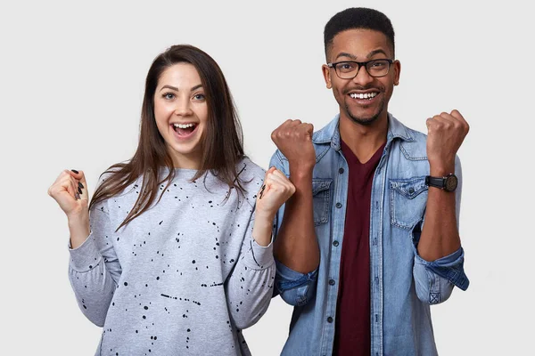 We can do it. Studio shot of happy couple clenching fists, celebrate victory, exclaim positively, looks glad, have cheerful faces, isolated over white background. People, success and triumph concept.