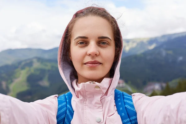 Beeld van goed uitziende tevreden reisblogger maken selfie, rusttijd, blij zijn met de omstandigheden van de reis, het krijgen van plezier door actieve rust, met bergen op haar achtergrond. Trip concept. — Stockfoto