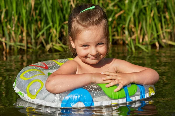 여름 방학 동안 휴식을 취하고, 수영 원으로 수영하고, 은행 근처의 강에서 휴식을 취하고, 더운 여름 날씨를 즐기고, 기뻐하는 작은 귀여운 아이. 어린이 및 수영 개념. — 스톡 사진