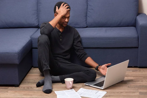 Porträtt av upptagen orolig man röra vid hans huvud med hand, med huvudvärk, cant förstå information som ges i nätet, med kopp med dryck och dokument i närheten, stanna hemma. Stress koncept. — Stockfoto