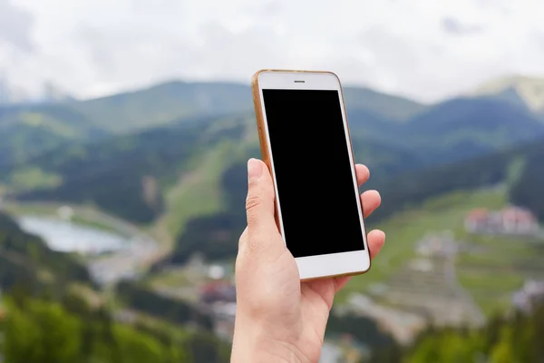 Gros plan photo de main inconnue tenant commuté smartphone avec écran blanc sur fond de montagne, à la recherche de connexion, va faire du selfie au sommet de la colline de montagne. Copyspace pour la publicité . — Photo
