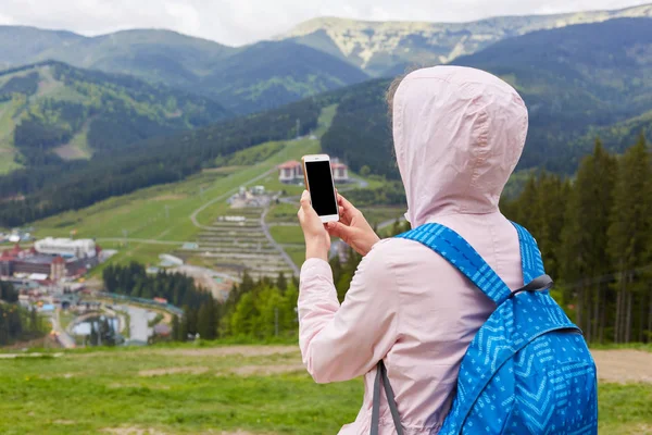 Vue arrière d'une femme mince tenant son smartphone dans les deux mains, prenant des photos pour le blog de voyage, à la recherche d'un nouvel itinéraire en ligne, à la recherche d'une connexion dans un tour de montagne. Copyspace pour la publicité . — Photo