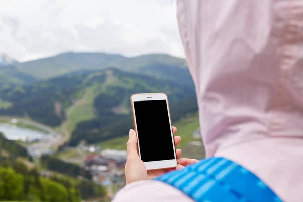 Vue arrière de la femme portant une veste rose et un sac à dos bleu, debout au sommet de la montagne, tenant son appareil, aucune image, à la recherche de connexion, va utiliser son smartphone. Copyspace pour la publicité . — Photo