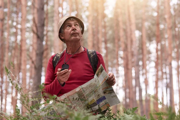 Colpo all'aperto di uomo anziano escursioni e guardando il cielo, tenendo bussola e mappa in mano, cercare di trovare la strada giusta, avendo riposo attivo e avventura nel legno, godendo della natura beaitiful. Concetto di viaggio — Foto Stock