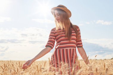 Güneşli bir günde yürüyen, buğday tarlasında olan, elleriyle saplara dokunan, hasır şapka giyen ve soyulmuş elbise giyen, doğadan zevk alan genç romantik kadın. İnsanlar ve doğa kavramı.