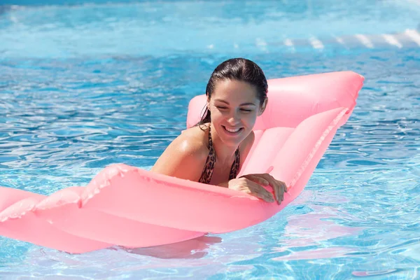 분홍색 물 매트리스의 도움으로 수영장에서 수영하는 재미 만족 여성의 초상화, 닫힌 눈과 진지한 미소로 휴식을 취하고 행복한 표정을 지었습니다. 수상 활동 개념. — 스톡 사진