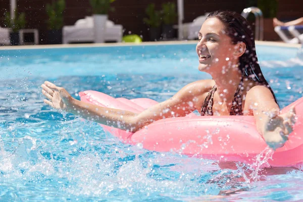 혼자 수영장에서 재미를 편안한 장난 여성의 야외 사진, 분홍색 물 매트리스에 누워, 물을 튀기, 높은 영혼에있는, 눈을 감고, 즐겁게 웃고. 워터 게임 컨셉. — 스톡 사진