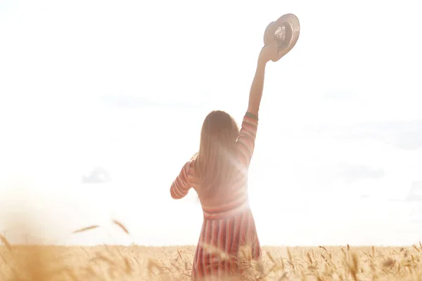 Tiro ao ar livre de menina com a mão para cima segurando seu chapéu de sol, divirta-se ao pôr do sol no campo, vestindo vestido, posando campo isolado e fundo do céu branco, bela natureza e paisagem, dia quente de verão . — Fotografia de Stock