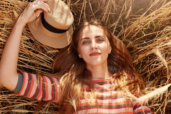 Close up retrato de jovem mulher atender por do sol e amanhecer no verão no campo de trigo, senhora atraente deitado em espiguetas no chão, olhando para a câmera. Conceito de felicidade, pessoas, natureza epaisagens . — Fotografia de Stock