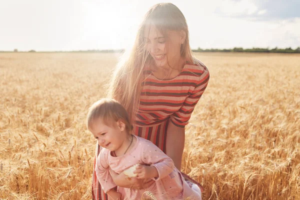 Little cheerful child having fun with her mother, holding bread in hands, enjoying her childhood. Happy playful mom holding her daughter in hands, entertaining her with game. Family concept. — Stock Photo, Image