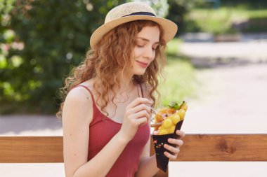 Sevimli sevimli genç bayan hoş yüz ifadesi olan, içtenlikle gülümseyen, ahşap çit yakınında tek başına açık havada oturan, tatlı tutan, kaşıkla yeme, onu yaz saati dinlenme zevk.