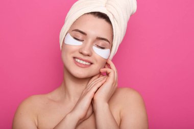 Neşeli huzurlu genç kadın hoş yüz ifadesi ne sahip, içtenlikle gülümseyen, kapalı gözlerle poz, elleriyle yüzüne dokunma, çıplak olma, yüzünde yamalar olan görüntü. Güzellik konsepti.