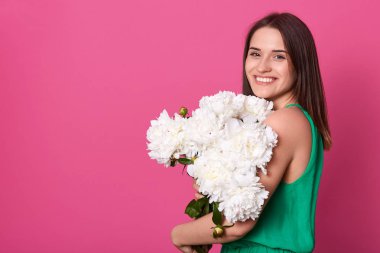 Çiçek demet tutan büyüleyici manyetik model Kapalı stüdyo çekim, samimi bir gülümseme olan, yeşil elbise giyen, şakayık güzelliği zevk, yüksek ruhları olmak. Reklam için copyspace.