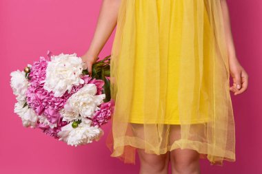 Parlak sarı elbise giyen bilinmeyen kadın Kapalı stüdyo çekim, beyaz ve pembe şakayık büyük buket tutan, mevcut alma, stüdyoda pembe arka plan üzerinde izole. İnsanlar ve çiçekler kavramı.