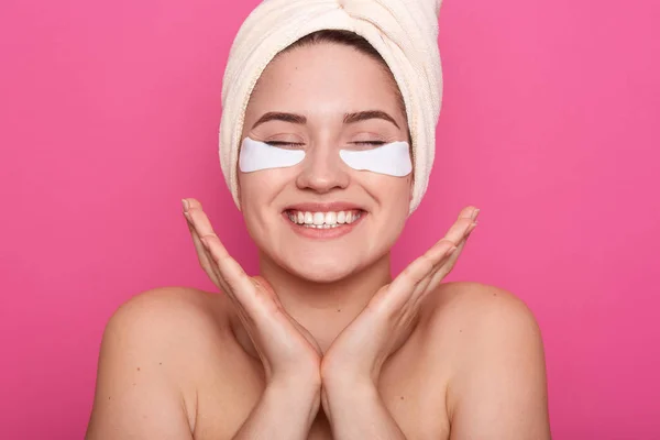 Indoor foto van positieve energieke Europese vrouw houden handen samen in de buurt van het gezicht, sluiten ogen, oprecht lachen, zijn dol op Beauty procedures, met patches onder de ogen, wachten op resultaten. — Stockfoto