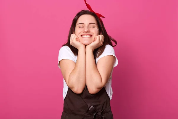 Jovem alegre encantada com expressão facial agradável, colocando as mãos no rosto, fechando os olhos, sorrindo sinceramente, gostando de fazer tarefas domésticas, estar em bom humor. Trabalhos domésticos . — Fotografia de Stock