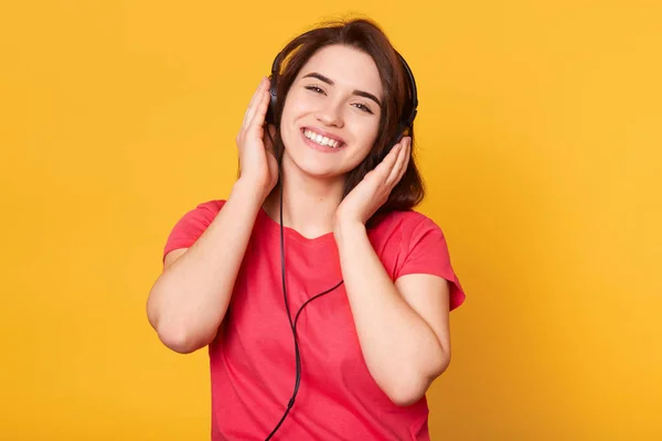 Bliska portret pozytywnego modelu magnetycznego pozowanie na żółto tle w Studio, słuchanie muzyki, uzyskiwanie przyjemności, uśmiechając się szczerze, patrząc bezpośrednio na kamerę. Koncepcja młodzieżowa. — Zdjęcie stockowe