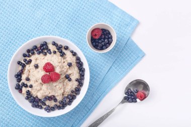 Çilek ve ahududu ile yulaf ezmesi derin plaka fotoğraf mavi pamuk havlu yatıyor hassas Beyaz ahşap arka plan üzerinde stand. Sağlıklı yemek, Kahvaltı, sağlıklı gıda ve diyet konsepti.