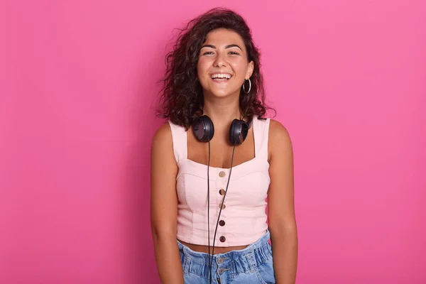 Imagen horizontal de una mujer escuchando música en un reproductor de mp3 o un teléfono inteligente. Fresca enérgica morena caucásica feliz posando aislada sobre fondo rosa. Copiar espacio para publicidad, promoción . —  Fotos de Stock