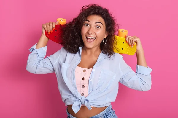 Halva längden foto av lycklig kvinna med mörkt lockigt hår, träffa vänner för ridning skateboard tillsammans, bär skjorta, t shirt och Jean, har smal figur, ha kul utomhus, med aktiv vila. — Stockfoto