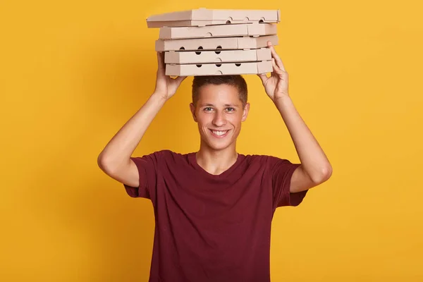 Primer plano retrato de joven repartidor alegre con camiseta roja de pie, sosteniendo pila de cajas de pizza de cartón sobre fondo gris. Interior, plano de estudio, aislado, espacio de copia . — Foto de Stock
