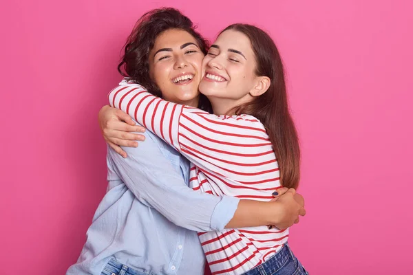 긍정적 인 여성, frienads 또는 자매가 서로 옆에 서서 따뜻한 포옹을하고, 핑크 색 배경 위에 고립 된 즐거운 미소로 포즈를 취하십시오. 우정과 행복의 개념. — 스톡 사진