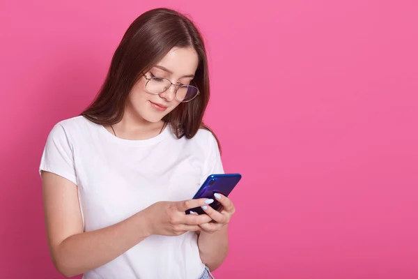 Beltéri shot fiatal jó kinézetű európai nő izolált rózsás háttér gazdaság kék telefon a kezében, és szeretnének a képernyőn, olvasás üzenetet a barátjával. Modern technológiai koncepció. — Stock Fotó
