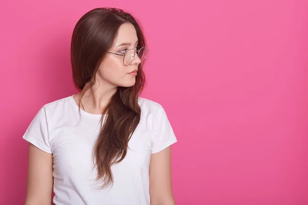 Perfil lateral retrato de mujer hermosa con el pelo largo, vestido blanco casual camiseta y gafas, mirando a un lado aislado ower fondo de estudio rosa con espacio de copia para su publicidad o promoción — Foto de Stock