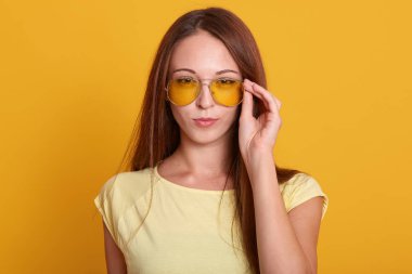 Sevimli kadın günlük kıyafet wering Yatay çekim, onu şık güneş gözlüğü el tutar, koyu uzun düz saçları olan, kurnaz yüz ifadesi ile kamera doğrudan bakarak. İnsan kavramı.