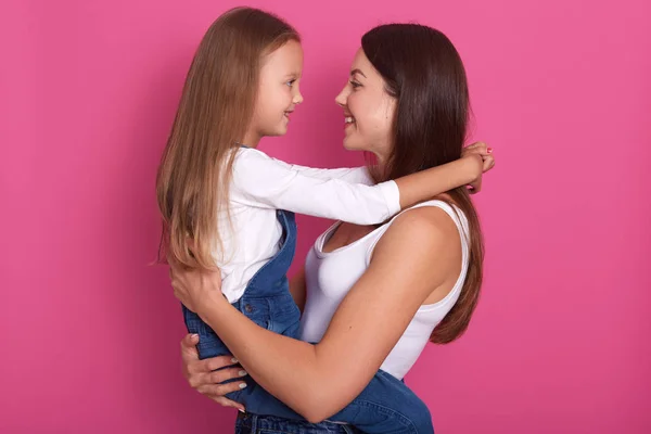 어머니와 딸은 서로를 보고, 엄마는 그녀의 매력적인 아이를 들고, 분홍색 스튜디오 배경 위에 고립 된 포즈 캐주얼 의상을 입고 여자 ang 소녀. 행복, 가족 및 사람 개념. — 스톡 사진