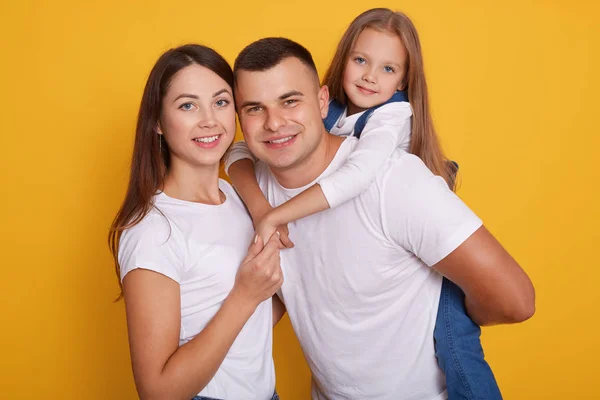 Portrait de parents heureux, papa porte leurs belles filles sur son dos. Belle famille de trois pose ensemble sur fond jaune, exprimant le bonheur. Jeune mère et père avec enfant — Photo