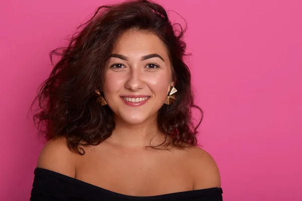 Fotografía horizontal de una hermosa mujer posando con los hombros desnudos, una mujer vistiendo una camisa negra, mirando sonriente a la cámara, de buen humor, aislada sobre un fondo de estudio rosa. Concepto de personas . —  Fotos de Stock