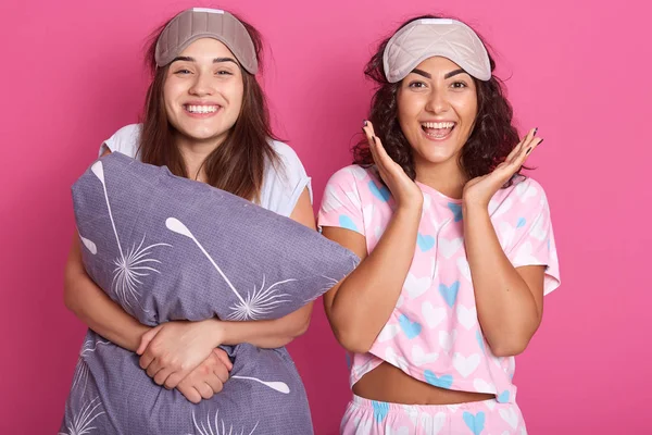 Εσωτερική βολή χαμογελαστών γυναικών με μάσκες ύπνου στο κεφάλι, φορώντας πιτζάμες που στέκονται απομονωμένες πάνω από ροζ φόντο στούντιο, έχοντας πιτζάμα πάρτι, κοιτάζοντας την κάμερα, έχουν καλή διάθεση. Έννοια της φιλίας. — Φωτογραφία Αρχείου