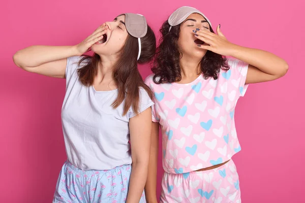 Εσωτερικό σφηνάκι από ελκυστικές νεαρές γυναίκες που στέκονται εναντίον του ροζ τοίχου στούντιο, διασκεδώντας μαζί, ποζάρισμα με μάσκα ύπνου και πιτζάμες, παίρνοντας τα στόματα με τα χέρια και το χιόνι. Έννοια της φιλίας. — Φωτογραφία Αρχείου