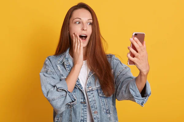 Nahaufnahme Porträt der netten schönen Frau beim Selfie, posiert vor gelbem Hintergrund, Dame mit offenem Mund hält ihr Handy, Mädchen trägt Hemd und stylische Jeansjacke. pe3ople-Konzept. — Stockfoto