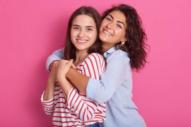 Gülümseyen kadınlar kucaklayan ve doğrudan kameraya bakıyor. Lezbiyen çift veya kadın arkadaşlık kavramı. Pembe arka plan üzerinde izole ön görünüm. Şık gömlek giyen bayanlar, hapyness ifade.